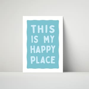 Pu&ograve; includere: Una stampa artistica incorniciata con le parole "THIS IS MY HAPPY PLACE" in lettere maiuscole blu chiaro su sfondo azzurro. La stampa &egrave; esposta su una superficie bianca.