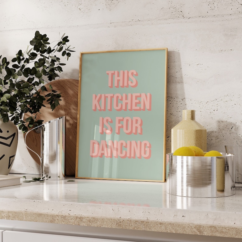 May include: A gold framed print with a light green background and the text "This kitchen is for dancing" in pink letters.