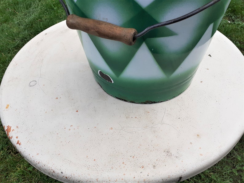 Puede incluir: Un cubo verde y blanco con un asa de madera sobre una superficie blanca. El cubo tiene un patr&oacute;n de diamantes.