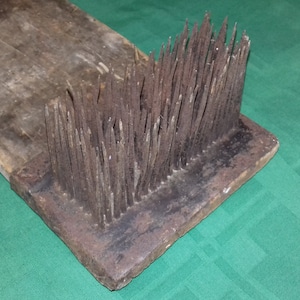 Peut inclure: Une planche en bois avec une rangée de dents en métal rouillées fixées à une extrémité. La planche est brune et les dents sont d'une couleur rouillée foncée.