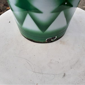 Puede incluir: Una mesa redonda blanca con un objeto cil&iacute;ndrico verde y blanco en la parte superior. El objeto tiene un patr&oacute;n geom&eacute;trico de tri&aacute;ngulos.