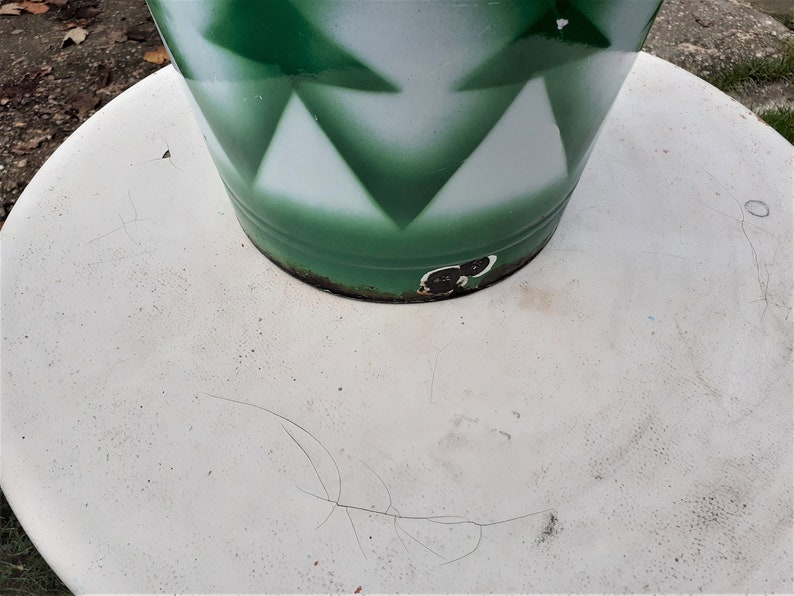Puede incluir: Una mesa redonda blanca con un objeto cil&iacute;ndrico verde y blanco en la parte superior. El objeto tiene un patr&oacute;n geom&eacute;trico de tri&aacute;ngulos.