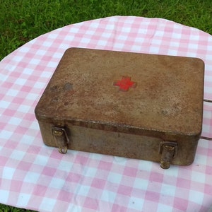 May include: A vintage metal first aid kit with a red cross on the lid. The kit is rusty and has a handle on the side.