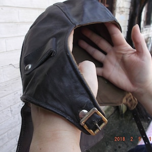 Peut inclure: Un chapeau d'aviateur en cuir noir avec une doublure marron et une boucle en laiton. Le chapeau a un rabat qui peut être rabattu pour couvrir les oreilles.
