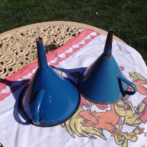 Op de afbeelding: Twee blauwe emaille trechters met handvatten. De trechters liggen op een witte handdoek met een rood-wit hartpatroon.