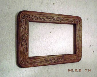 May include: A wooden picture frame with a carved design of swirling leaves and vines. The frame is a dark brown color and has a rectangular shape.