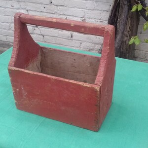 May include: A red wooden carrying case with a handle. The case is made of wood and has a rustic look.