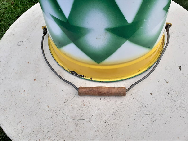 Puede incluir: Un cubo de metal vintage con un patr&oacute;n de diamantes verde y blanco y un borde amarillo. El cubo tiene un asa de alambre con un agarre de madera.