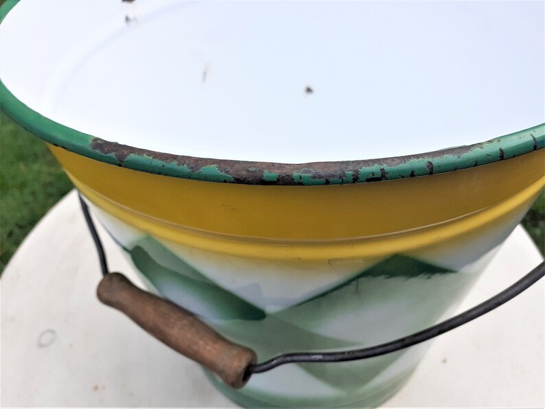 Puede incluir: Un cubo de esmalte vintage con un dise&ntilde;o amarillo, blanco y verde. El cubo tiene un asa de madera y un borde de alambre met&aacute;lico.