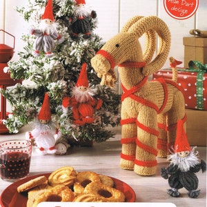 May include: A festive scene featuring a decorated Christmas tree with gnome ornaments and a knitted goat figure. A plate of cookies and a glass of red liquid are in the foreground. Text reads "Go Scandi!"