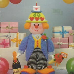 May include: A knitting pattern booklet titled Jean Greenhowe's Celebration Clowns The Red Nose Gang Part Two. The cover features a knitted clown wearing a yellow hat with a cake, a blue jacket, and striped trousers, holding a bottle and flowers.