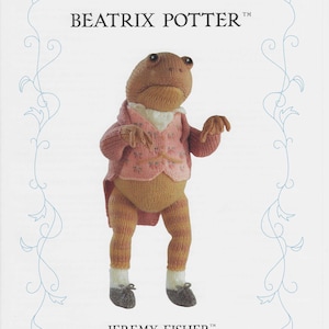 May include: A knitted toy frog wearing a pink waistcoat and brown trousers. The frog is standing on a white background with the text "The World of Beatrix Potter" and "Jeremy Fisher" in black.