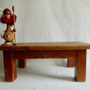 Könnte beinhalten: Eine Holzfigur eines Wikingers mit rotem Bart und Hörnerhelm steht auf einem kleinen, rechteckigen Holztisch. Der Tisch ist dunkelbraun gebeizt und hat vier Beine. Die Figur hält einen Holzspeer.