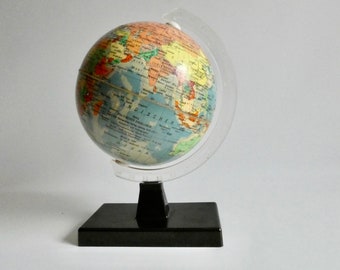 May include: A colorful globe with a detailed map of the world, mounted on a black rectangular base. The globe is held in place by a clear plastic meridian ring. The continents are depicted in various colors.