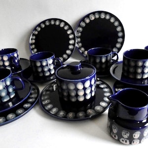 Könnte beinhalten: Ein komplettes Set aus dunkelblauem Keramikgeschirr mit weißem Punktmuster. Das Set umfasst Teller, Untertassen, Tassen, einen Sahnekännchen und eine Servierschüssel mit Deckel. Das Geschirr ist auf einer weißen Oberfläche angeordnet.