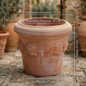 Może przedstawiać: Terakotowa donica z dekoracyjnym wzorem liści. Donica ma średnicę zewnętrzną 25 cm, średnicę wewnętrzną 20 cm, wysokość 23 cm i podstawę 17 cm. Donica nadaje się do użytku na zewnątrz.