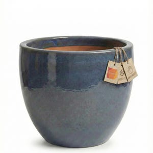 Può includere: Un grande vaso in ceramica smaltata blu, di forma arrotondata. Il vaso ha una finitura lucida e un'ampia apertura. Piccole etichette sono attaccate al vaso. Adatto per uso esterno.