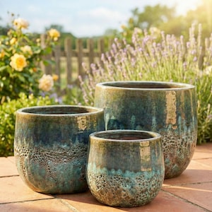 May include: Three glazed ceramic planters in varying sizes. The planters have a textured, mottled finish in shades of teal, blue, and brown. They are set on a brick patio with a garden background.