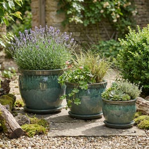 May include: Three glazed teal ceramic planters of varying sizes, each filled with different plants. The largest pot holds lavender, the middle one has ornamental grass and the smallest has succulents. All sit on matching saucers.