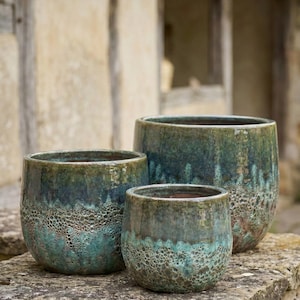 May include: Three ceramic planters in varying sizes, featuring a textured, mottled glaze in shades of teal and green. The planters have a rounded shape and sit on a stone surface, suitable for outdoor use.