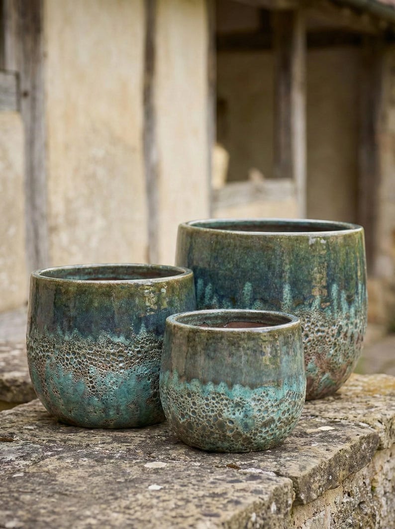 May include: Three ceramic planters in varying sizes, featuring a textured, mottled glaze in shades of teal and green. The planters have a rounded shape and sit on a stone surface, suitable for outdoor use.