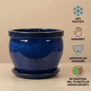 May include: A glossy, deep blue ceramic planter with a matching saucer. The round pot has a wide opening and a slightly curved body. The image includes text indicating it is frost-resistant, handmade, and suitable for indoor use.
