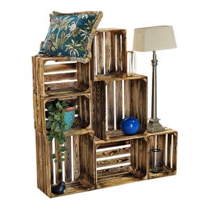Può includere: Scaffalatura rustica in casse di legno con vari oggetti decorativi. Include una lampada, una palla blu, un cuscino floreale e una pianta in vaso. Lo stile è un mix tra rustico e vintage. L'altezza è di circa 150 cm.