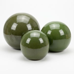 May include: Three glossy, olive-green decorative spheres of varying sizes. The spheres have a smooth, reflective surface, and are arranged together. The largest sphere is in the background, with the smallest sphere in front.