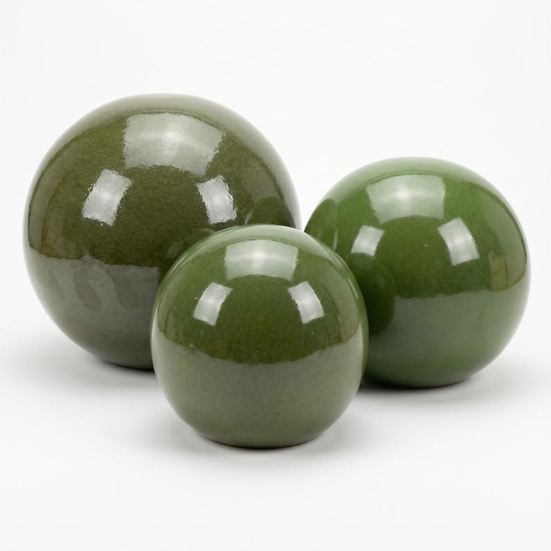 May include: Three glossy, olive-green decorative spheres of varying sizes. The spheres have a smooth, reflective surface, and are arranged together. The largest sphere is in the background, with the smallest sphere in front.