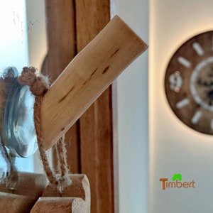 May include: A close-up of a wooden bottle stopper with a rope tied around it. The stopper is made of light-colored wood with visible grain. The rope is brown and has a knot at the end. The stopper is in focus, while the background is blurred.