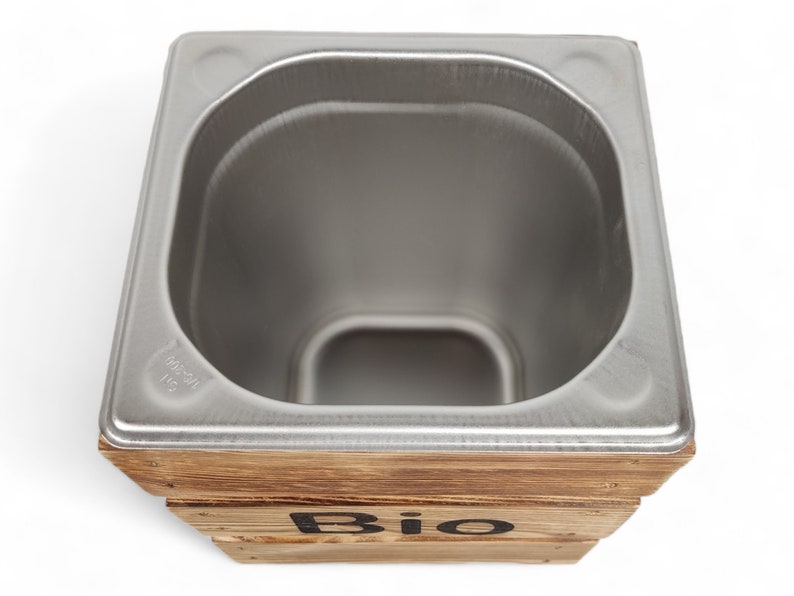 May include: A stainless steel compost bin with a wooden frame. The bin has a rounded top and the word "Bio" is printed on the front of the frame.
