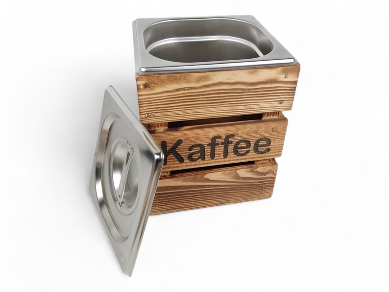 May include: A wooden box with a stainless steel lid and the word "Kaffee" printed on the front. The box is made of natural wood with a rustic finish.
