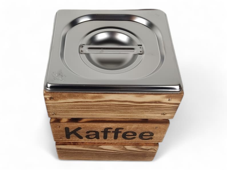 May include: A wooden box with a stainless steel lid, labeled "Kaffee". The box is made of natural wood with a rustic finish.