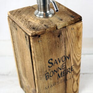 May include: A wooden soap dispenser with a stainless steel pump. The dispenser is made from reclaimed wood and has the text "Savon Bonne Mere Marseille" printed on the front.