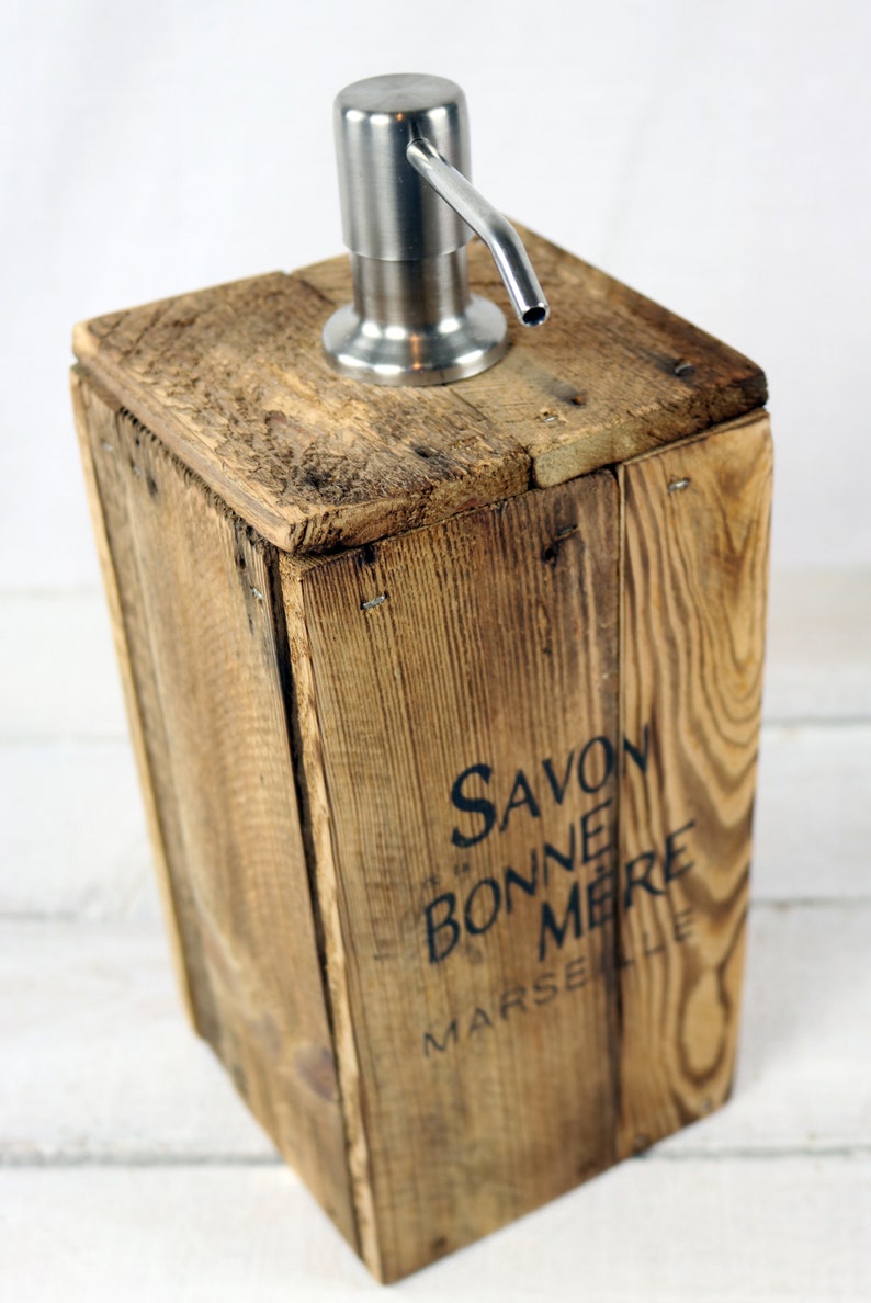 May include: A wooden soap dispenser with a stainless steel pump. The dispenser is made from reclaimed wood and has the text "Savon Bonne Mere Marseille" printed on the front.