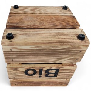 May include: A wooden box with a black label that says "Bio!" The box is made of natural wood and has a rustic look. It has black rubber feet on the bottom.