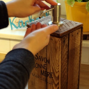 May include: A wooden soap dispenser with a stainless steel pump. The dispenser is labeled "Savon Bonne Mere Marseille".