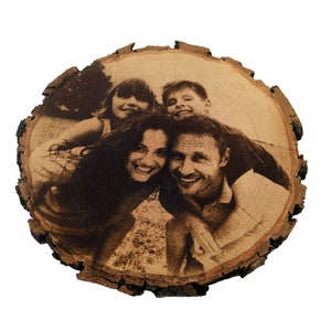 May include: A wood slice with a burnt-in image of a family of four smiling. The family is made up of two parents and two children. The image is in black and white.