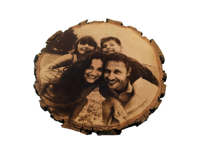 May include: A wood slice with a burnt-in image of a family of four smiling. The family is made up of two parents and two children. The image is in black and white.