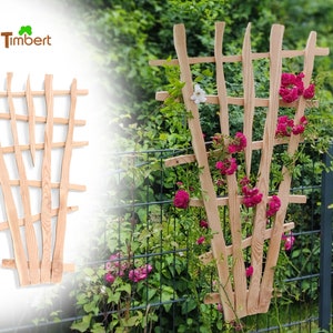 Puede incluir: Un enrejado de madera con un patrón de diamante, perfecto para plantas trepadoras. El enrejado está hecho de madera natural y tiene un aspecto rústico. Se muestra frente a un arbusto verde con flores rosas.