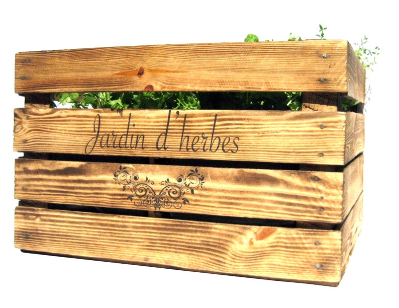 May include: A wooden crate planter with the text "Jardin d'herbes" and a decorative design. The planter is filled with green herbs.