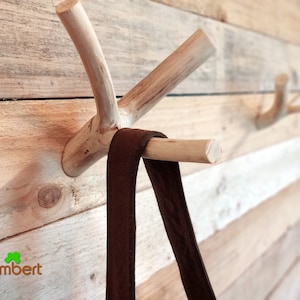 May include: A wooden wall mounted coat rack with multiple branches, each with a hook at the end. A brown leather strap hangs from one of the hooks.