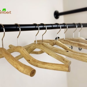 Op de afbeelding: Een set houten hangers met een natuurlijke afwerking, hangend aan een zwarte metalen pijp. De hangers zijn gemaakt van takken en hebben een unieke, rustieke uitstraling.