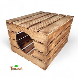 Può includere: Un letto per gatti in legno con un'apertura rotonda nella parte anteriore. Il letto è realizzato con assi di legno naturale e ha una finitura marrone rustica. Il letto è su una superficie bianca. Il testo "Timbert" è visibile nell'angolo in basso a sinistra dell'immagine.