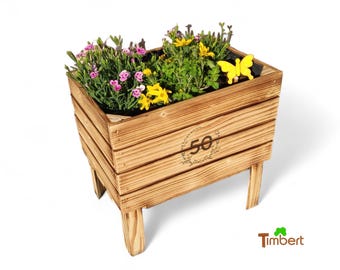 May include: A wooden planter box with a 50th anniversary logo, featuring pink and yellow flowers and a yellow butterfly. The planter is on four legs and is made of natural wood.