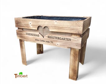May include: A rectangular wooden planter with a heart-shaped cutout and the text "THERESIAS KRÄUTERGARTEN" and "Alles Liebe zum 70." The planter has four legs and a dark interior. The wood has a natural, light brown finish.