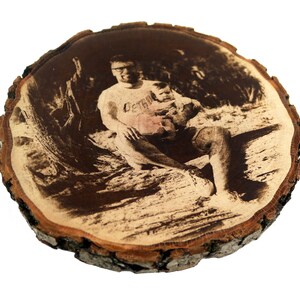 May include: A black and white photo of a man and a child is printed on a round wooden slice. The man is wearing a t-shirt with the word "Certain" printed on it.