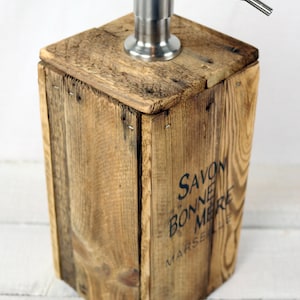 May include: A wooden soap dispenser with a stainless steel pump. The dispenser is made from reclaimed wood and has the text "SAVON BONNE MERE MARSEILLE" printed on the side.