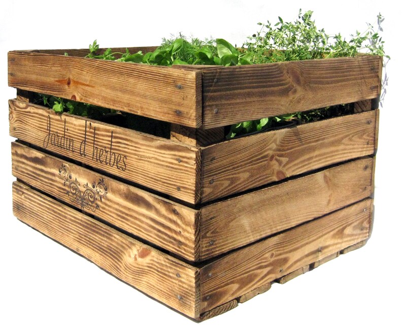 May include: A wooden crate planter with the text "Jardin d'herbes" inscribed on the side. The planter is filled with various herbs, including thyme, parsley, and dill.