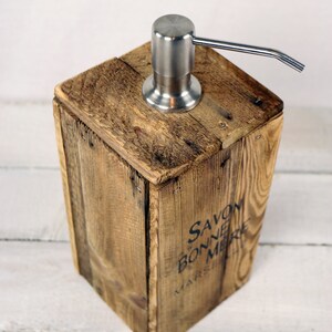 May include: A wooden soap dispenser with a stainless steel pump. The dispenser is made from reclaimed wood and has the words "Savon de Bonne Mere Marseille" printed on the side.